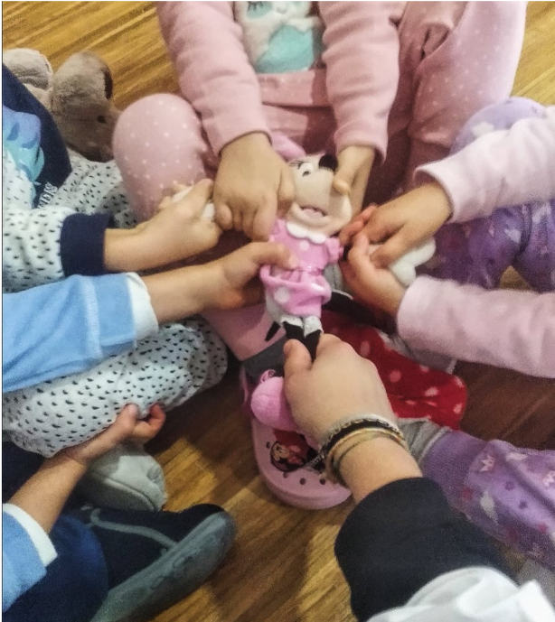 Crianças sentadas, disputando uma boneca